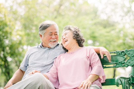 Happy Asian Senior couple laughing while sitting on the bench in the parkの写真素材