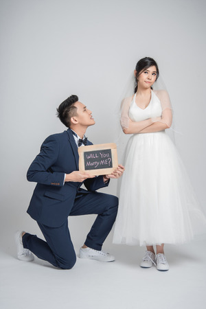 Asian man down on his knee and hold will you marry me? sign to ask his girlfriend on white backgroundの写真素材
