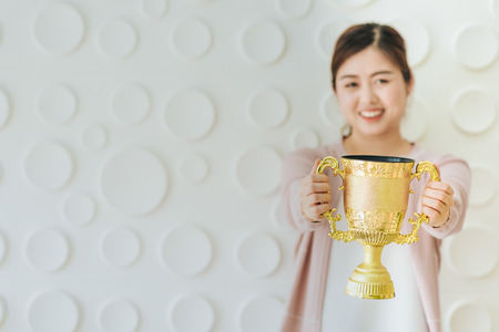 Happy Asian woman present gold trophy to celebrate successの写真素材
