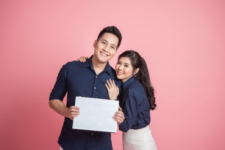 Happy young Asian couple holding blank banner isolated on pink backgroundの写真素材