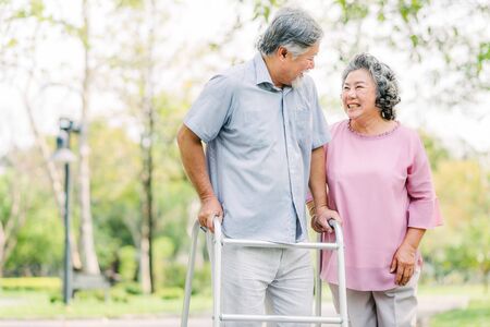 Portrait of happy loving senior Asian couple laughing while walking with walker in the parkの写真素材