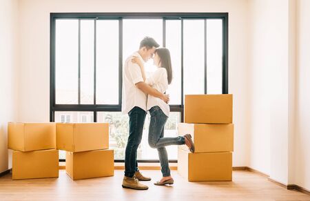 Full length shot of an affectionate young Asian couple embracing in their new home on moving dayの写真素材