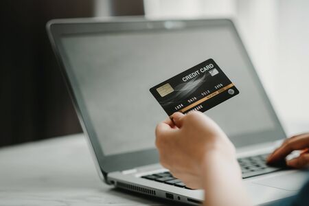 Close up shot of hand holding credit card while using laptop in background. Online shopping, payment conceptの写真素材
