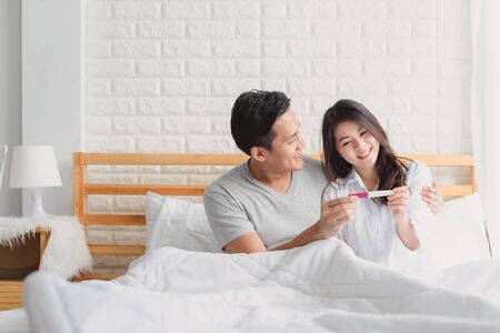 Happy Asian couple smiling after find out positive pregnancy test in bedroom at home: Royalty-free images, photos and pictures