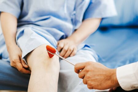 Doctor checking reflexes of a patient on the knee with reflex hammerの写真素材