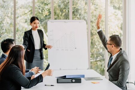 Businessman raising his hand up to share his opinion during business team meeting in conference room in modern officeの写真素材