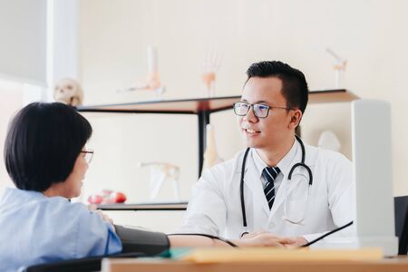Asian doctor talking to senior woman patient in office while checking blood pressureの写真素材