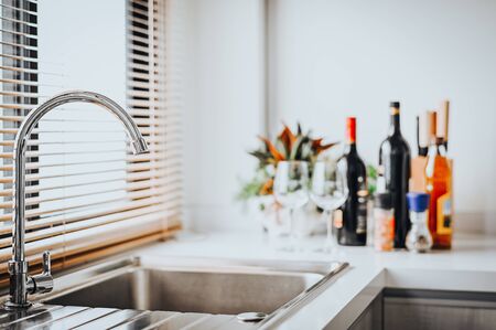 Close up shot of stainless steel faucet in a modern kitchen with bottle of wine in background の写真素材