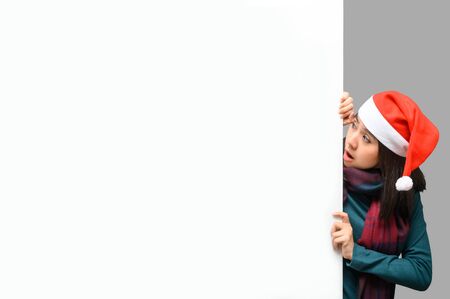 Asian woman peeking over white advertisement banner background with copy space wearing santa Christmas hat.の写真素材