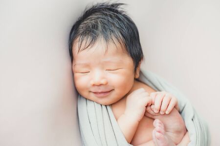Smiilng adorable Asian newborn baby sleeping in blanket on bedの写真素材