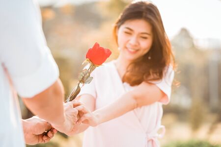Beautiful romantic couple in love moment. Man giving a rose to woman on valentine day she feeling shy. picture focused on roseの写真素材