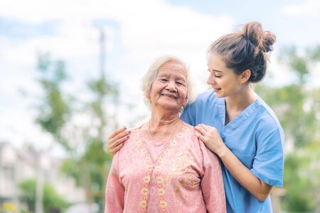 Smiling nurse caregiver take care of Asian elderly woman outdoor in the parkの写真素材