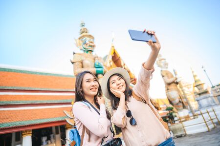 Happy young tourist women friends enjoy taking selfie together while travel in temple of the emerald buddha, Wat Phra Kaew, popular tourist place in Bangkok, Thailandの写真素材