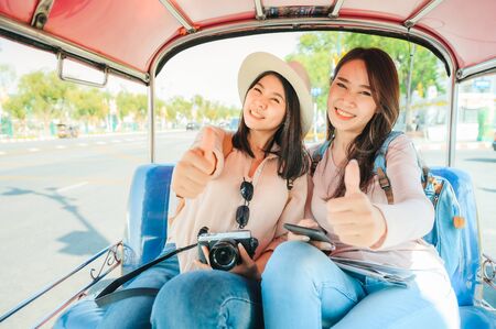 Two Happy Asian girls best friends traveler sit in Tuk Tuk taxi showing thumb up and having fun road trip while vacation in bangkok, Thailandの写真素材