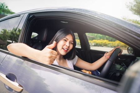 Happy smiling asian woman driving her new car and showing thumb up. with confidentの写真素材