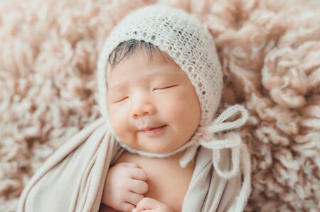 An adorable cute smiling Asian newborn baby with knitted hat and wrapprd in cocoon sleeping on furの写真素材