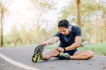 Close up shot of athlete runner young Asian male stretching his leg on race track in the park