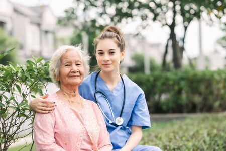 Nurse caregiver embracing happy Asian elderly woman outdoor in the park. Focused on eldery womanの写真素材