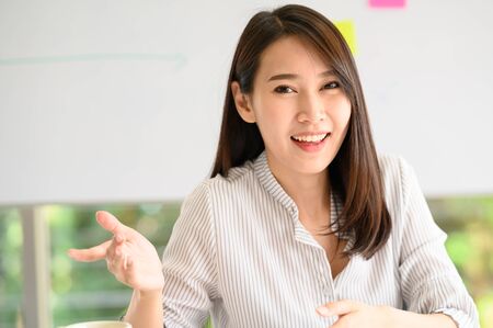 Happy smiling Asian woman explaining something to her colleague during video call meetingの写真素材