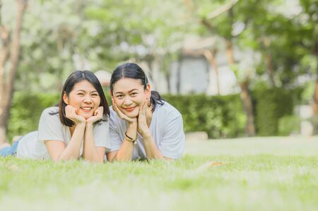 Two happy best friends Asian women lying on green grass outdoor in the park.の写真素材
