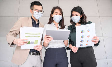 Asian business people entrepreneur wears face mask discuss project in tablet and paper in meeting room at modern officeの写真素材