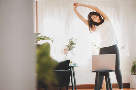 Asian woman doing plank exercise at home in a living room while watching online workout session from...