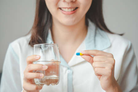 Close up shot of smiling woman holding capsule pill and glass of water. Image focused on capsule