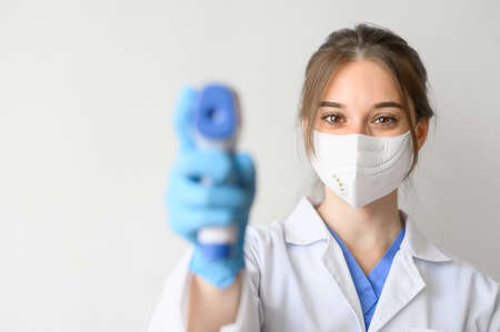 Female doctor wearing protective mask using infrared thermometer to check body temperature on white backgroundの写真素材