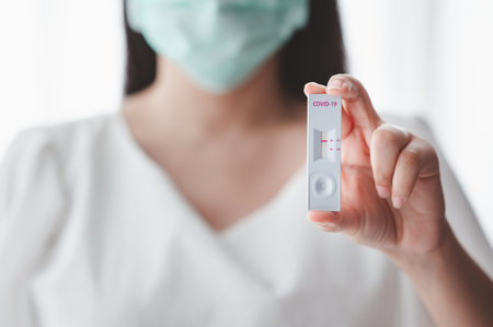 Close up shot of women wearing medical face mask showing covid-19 test strip with negative result in handの写真素材