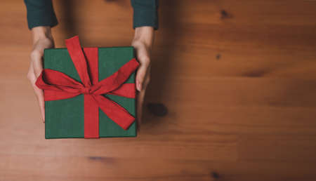 Top view of woman hand holding green Christmas gift box presents on a wooden table background