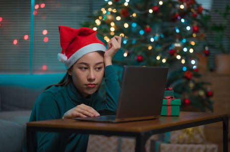 Happy Asian woman showing presents gift box to camera on laptop during chirstmas or new year holidays. Online celebration at homeの写真素材