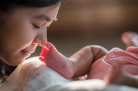 Happy asian laughing mother lifting her adorable 3 moths baby girl in air on sofa in living roomの写真素材