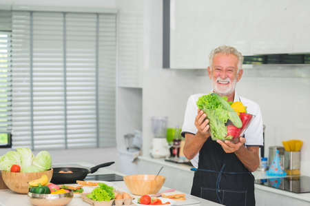 Happy smiling senior Caucasian man holding vegetables in kitchen at home. Healthy lifestyleの写真素材