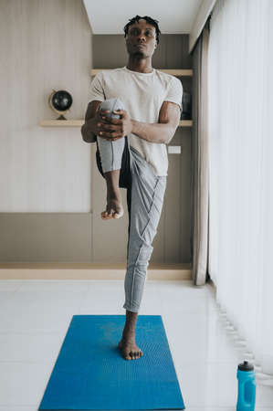 Black Man doing leg stretching exercise at home. workout at homeの写真素材
