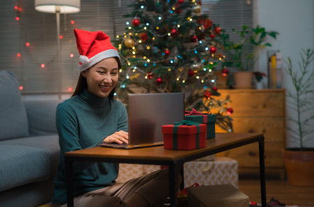 Asian woman wearing Christmas hat drinking champagne video call celebrate Happy New Year party online with her friends or family via laptop at homeの写真素材