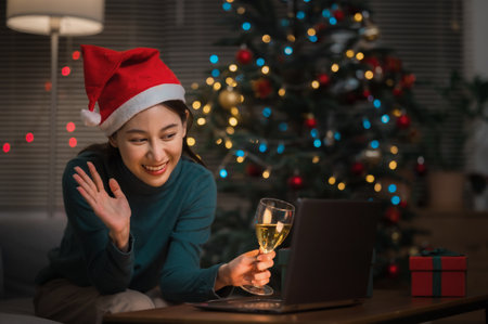 Asian woman wearing Christmas hat drinking champagne video call celebrate Happy New Year party online with her friends or family via laptop at homeの写真素材