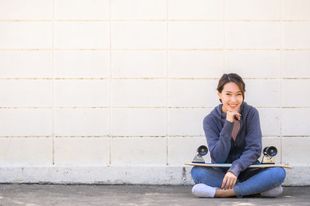 Happy smilling Asian woman relax sitting oustside with skateboard on lapの写真素材