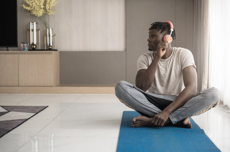 African man wearing sport outfit using headphone to listen music while exercise workout at home for good healthの写真素材