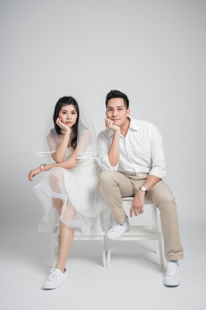 Happy young couple Asian groom and bride in casual wedding dress sitting on chairの写真素材
