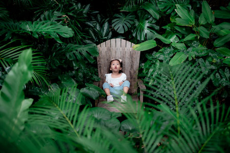 happy cute little happy Asian child girl exciting to see forest with green leaves while sitting on...