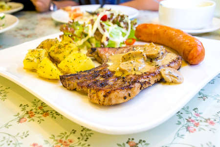 Grilled steaks with sausage, baked potatoes and vegetablesの写真素材