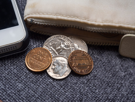 US dollar coins placed outside the wallet with smartphone.
