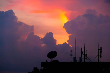 silhouette satellite dish and antenna communication over sunset sky in cityの写真素材