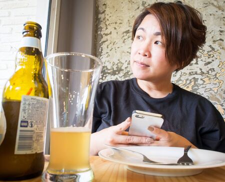 Asian woman chat on smartphone while drinking beerの写真素材