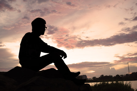 man sitting on rock watching the sunsetの写真素材