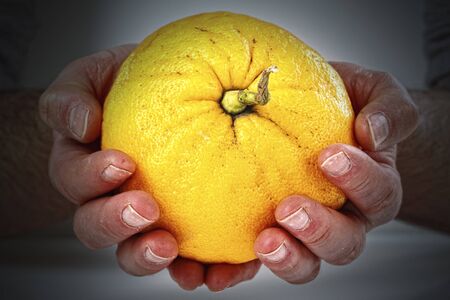 old hands holding grapefruit on dark backgroundの写真素材
