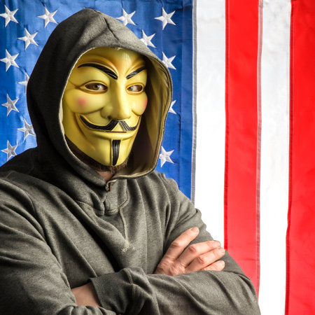 MILAN,ITALY, February, 2018: Hacker crossing arms wear anonymus mask with american old glory flag in background.Editorial photo.のeditorial素材