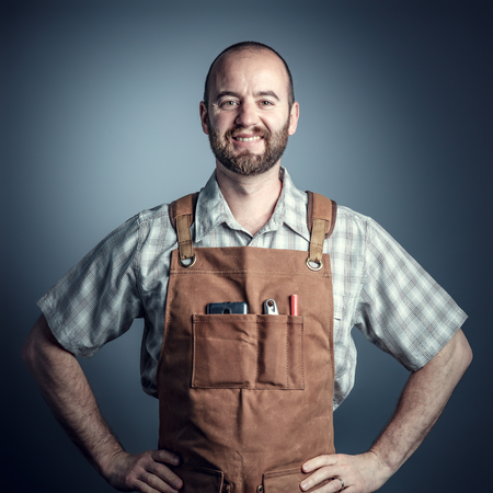 smiling caucasian carpenter with apron, studio shot portraitの写真素材