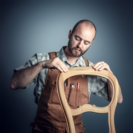 portrait of carpenter checking unfinished wood chair,studio shotの写真素材