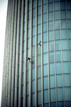 AMMAN, JORDAN - MARCH 12, 2019: Two window cleaners work on the facade of a skyscraper in the center of Amman, one of them uses a smartphone.のeditorial素材